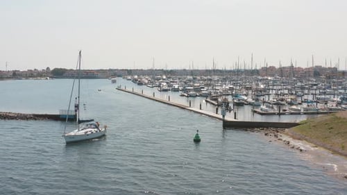 Cinematic drone / aerial shot of a boat sailing on the ocean with a marina in the background with sa
