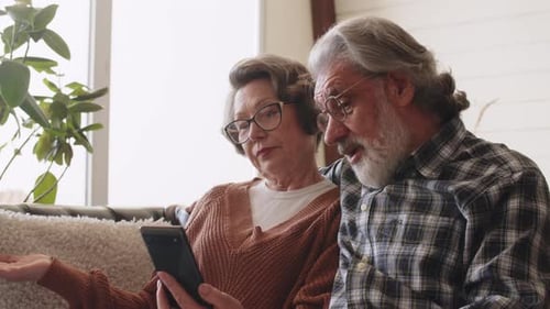 Senior Couple Using Smartphone Together on Sofa