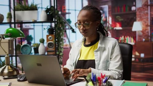 Teleworker Analyzing Data on Laptop at Desk and Looking Over Paperwork