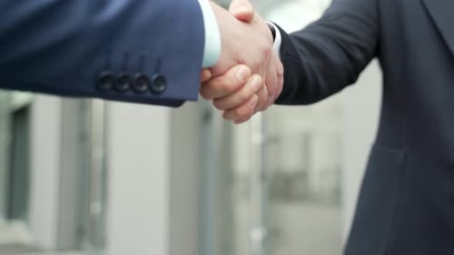 Close up business people shaking hands partnership deal while standing outside on the street near