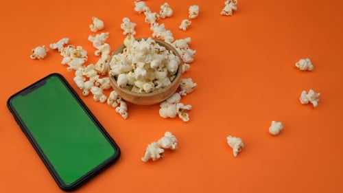 Smartphone with Green Screen Next to Popcorn Bowl