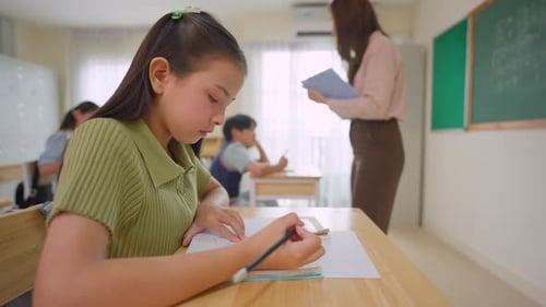 Asian student learning with teacher in classroom at elementary school.