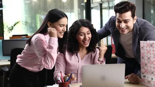 Cheerful Office Colleagues looking at laptop clenching their fists and celebrating their success