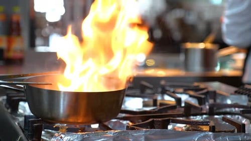 Close-up of a Restaurant Chef Cooking Food on Fire in the Restaurant Kitchen
