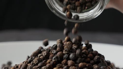 Dried Whole Black Peppercorns Poured Into The Plate. - closeup shot