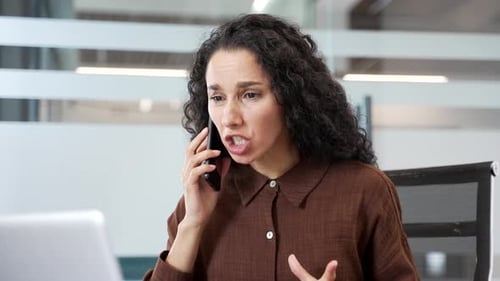 Angry businesswoman arguing talking on mobile phone at workplace in office. Frustrated female