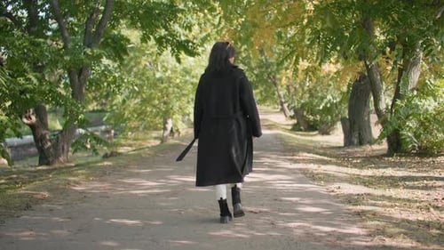Back View of Girl Walking in Arboretum Path Under Green Trees