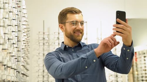 Bearded Man Browsing with Smartphone in Optometrist's Office