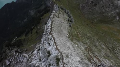 Drone shot tilting up, revealing the long and massive mountain ridge covered in snow that fades away
