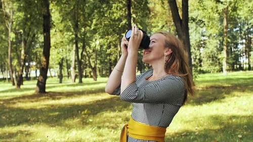 A Young Girl Photographer with a Camera Poses in the Park