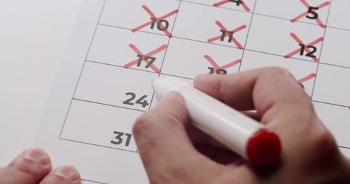 Hand Crossing Out Dates on Calendar with Marker