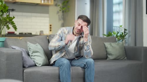 Young Man with Headache Sits on Couch