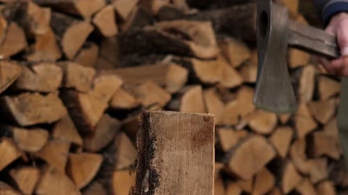 Closeup of a Man Chopping Wood with an Axe in the Backyard of a House