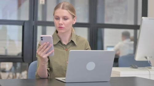 Woman Using Phone and Laptop in Modern Office