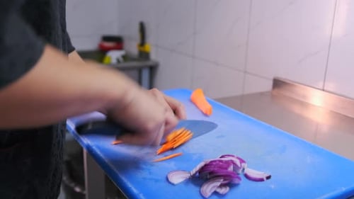 Hands of chef cutting fresh orange carrot on a cutting board in a restaurant kitchen. Close up.