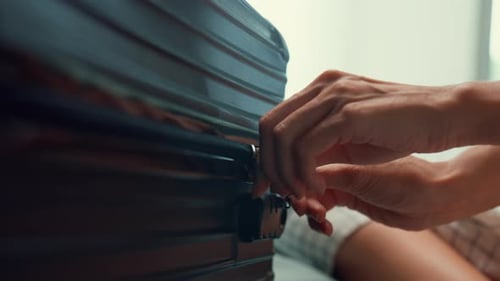 Asian female ready for summer holidays prepare black suitcase finish packing close zip bag on bed.