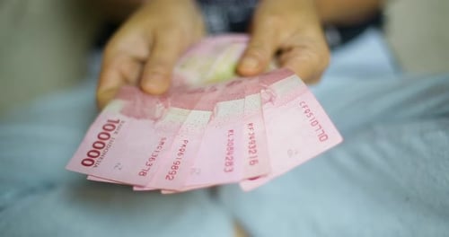 An Asian female hand is holding bunches of Indonesian Rupiah (IDR) Red 100,000 bank notes currency.