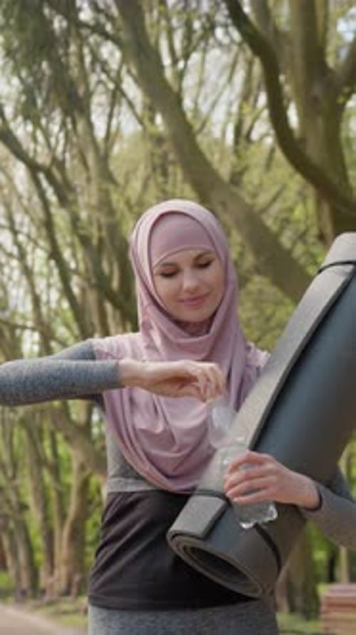 Young Woman Drinking Water With Yoga Mat in Park