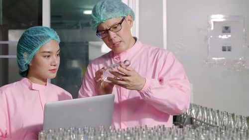 Deux ingénieurs supervisent le contrôle qualité en vérifiant les bouteilles de produits sur le tapis roulant d'une usine de boissons