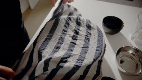 Young Female placing a wet towel on a bowl with dough for a cake in the kitchen at home. Homemade pa