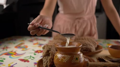 Woman Stirring Leche with Cinnamon Next to Pan Dulce