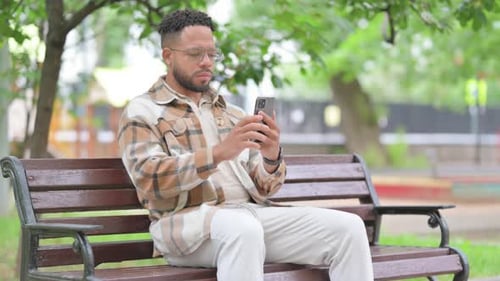 Man Uses Smartphone While Sitting on Park Bench