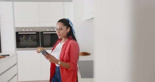 Woman Enjoys Snack While Using Smartphone in Kitchen