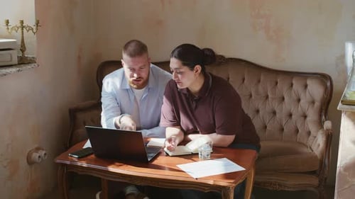 Two Colleagues Working by Laptop Sitting on Sofa in Vintage Cafe