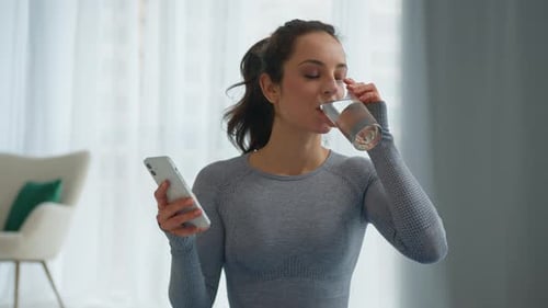 Woman Using Phone While Drinking Water Indoors