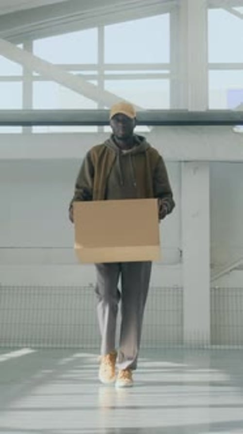 Vertical of African American Man with Cardboard Box Walking Along Storage Room
