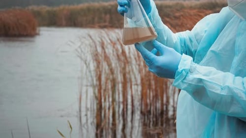 Side View Of Young Student Scientist Looks At Polluted Water In Test Flask And Evaluates Pollution