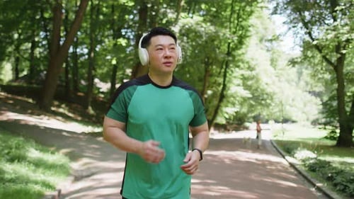 Active Sportsman Jogging Training Marathon Run Listening to Music in Wireless Headphones in Park