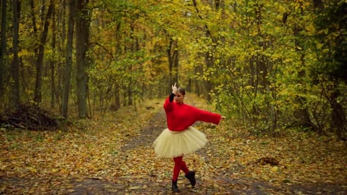 A Small Woman in a Bright Outfit is Dancing in a Large Autumn Forest
