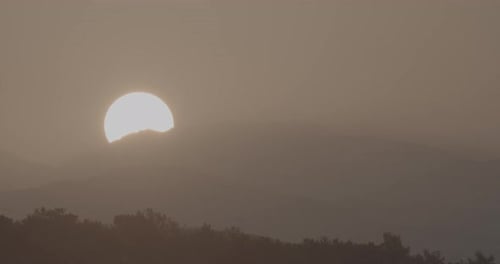 Sun Rises Behind Mountain Peaks in Hazy Sky