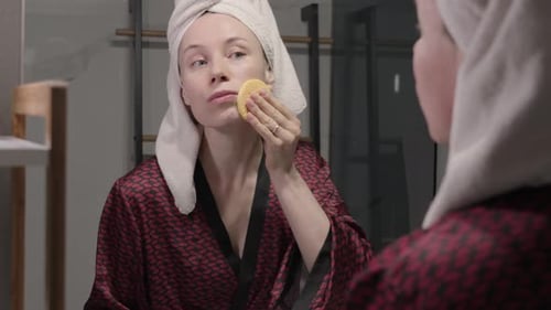 Woman Exfoliating Face in Bathroom Mirror
