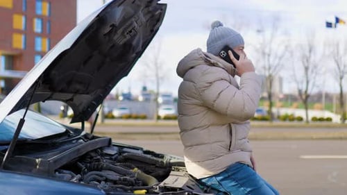 A Lone Man Looking Unhappy and Stressed Stands By His Damaged Vehicle on the Side of the Road