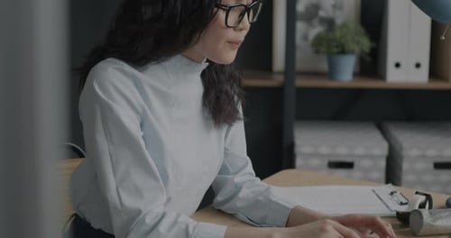 Elegant Asian Office Worker Using Laptop Typing and Touching Eyeglasses at Desk in Office