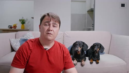 Man Sits on Couch with Two Dogs