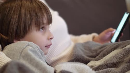 Child with Mother Relaxing with Phone on Sofa