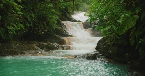 Cascading stepped waterfall flows into a vibrant turquoise pool in deep jungle setting of Costa Rica