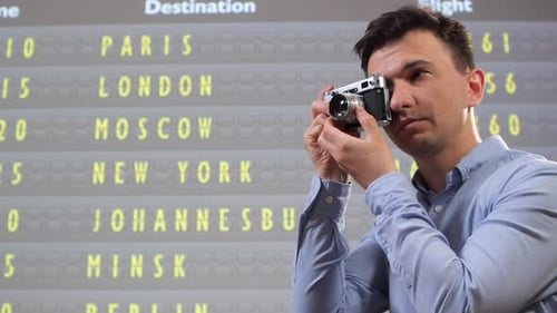 Man Holding Old Film Camera Capturing Information From a Split Flap Display Board Showing Various
