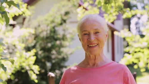 Happy smiling senior woman enjoying summer sunshine in her garden home