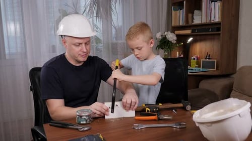 Focused Child and Adult Sawing Wood at Table