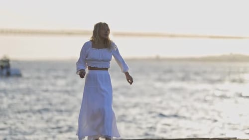 A Woman in a White Dress is Dancing on a Pier Overlooking the Water