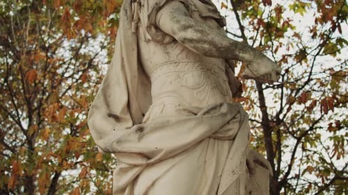 Tilt shot of Julius Caesar statue surrounded by colorful fall leaves in a park setting.