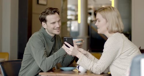 Young Adult couple discussing over mobile phone at table in cafe together