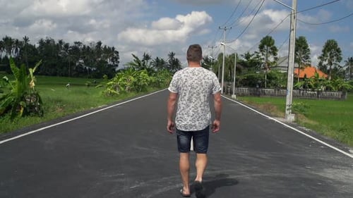 Young man strolling on a rural country road in summer enjoying a carefree day