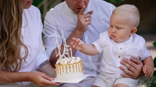 Parents sit holding a baby and a birthday cake in front of him.