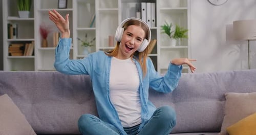 Enthusiastic Woman Dancing with Headphones on Sofa