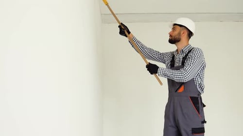 Construction Worker Paints Wall with Roller in Bright Room